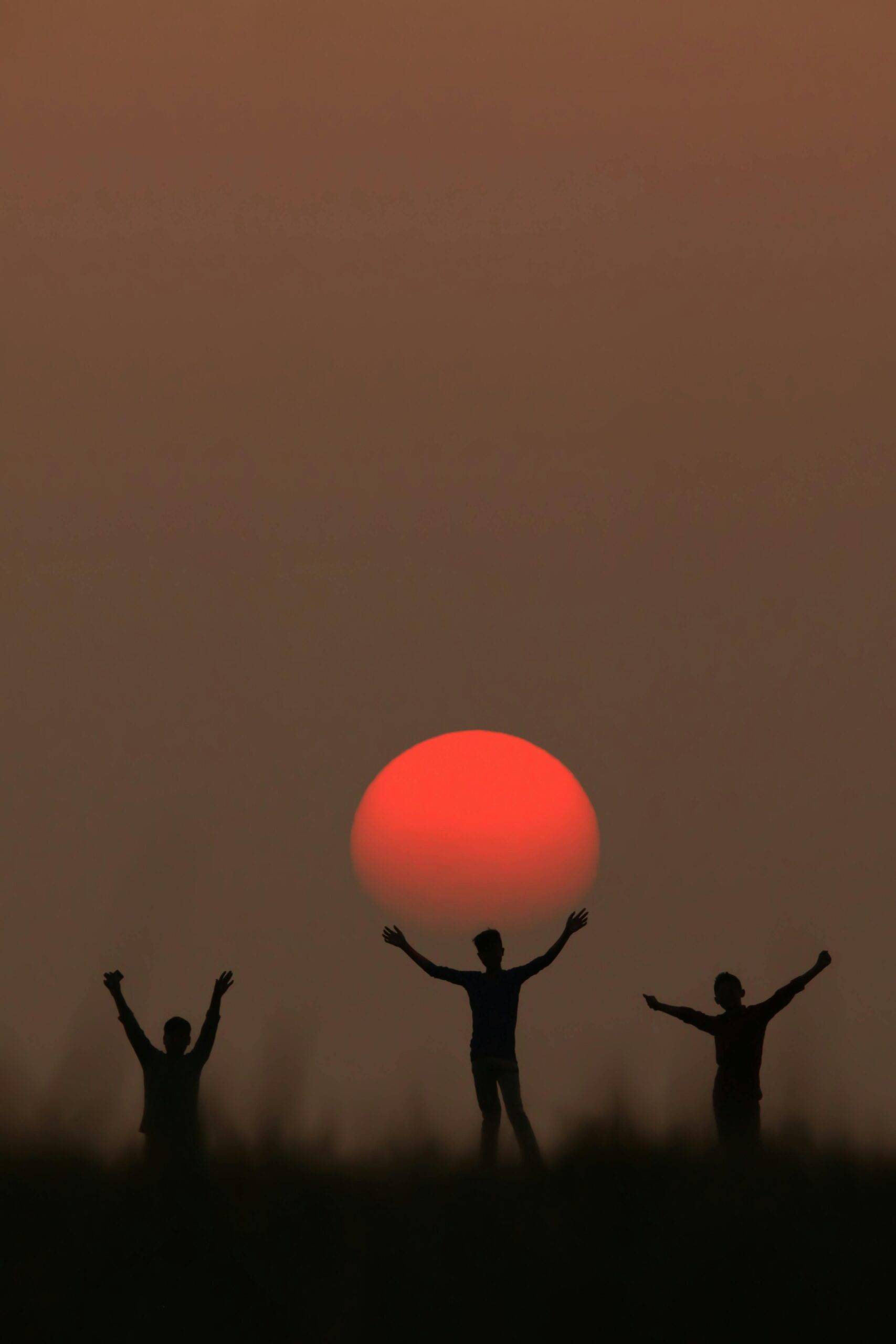 Silhouette of three people with raised arms against the sunset in Sitakund, Bangladesh.